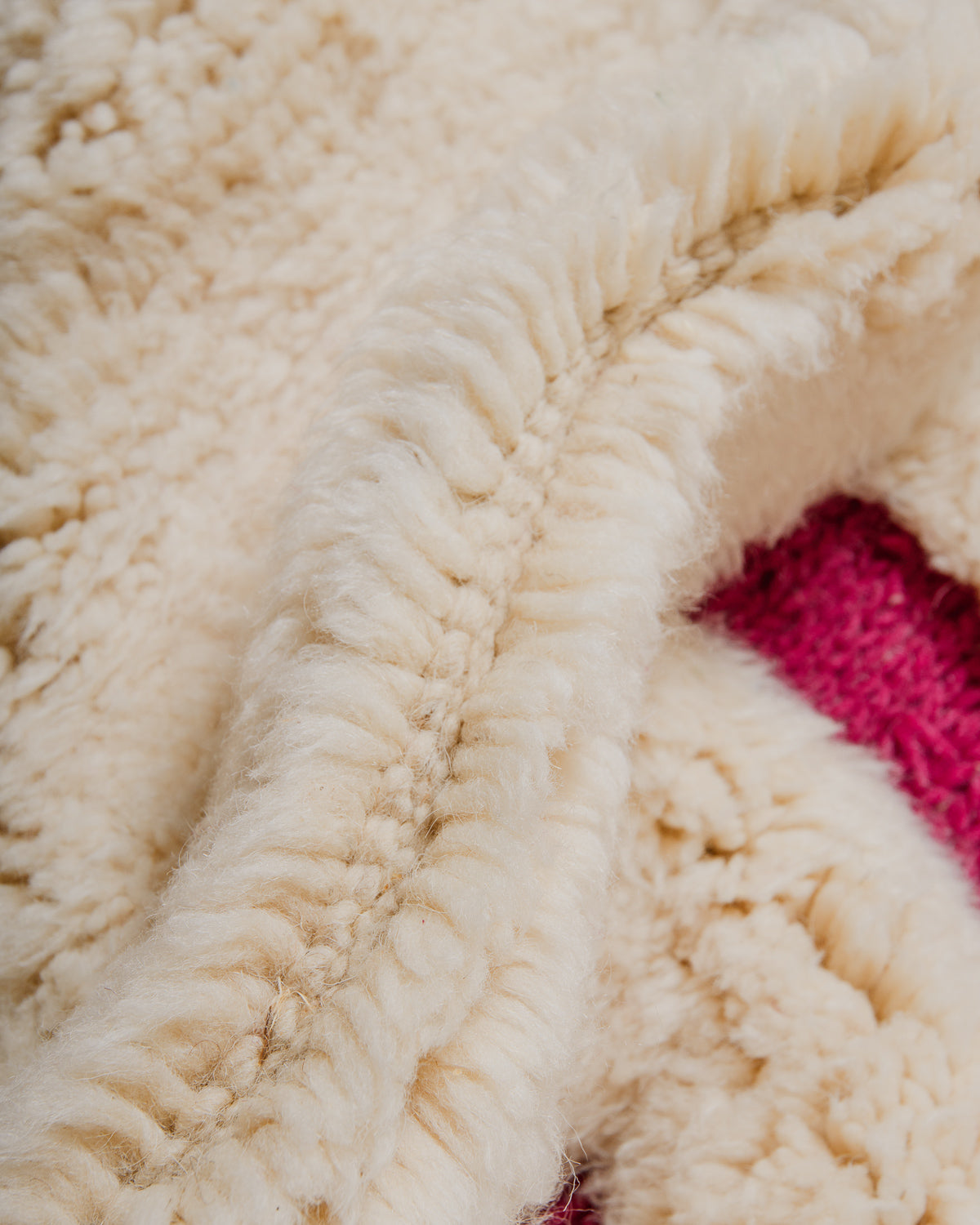 Close up of cream and magenta rug with thick pile and woven areas.